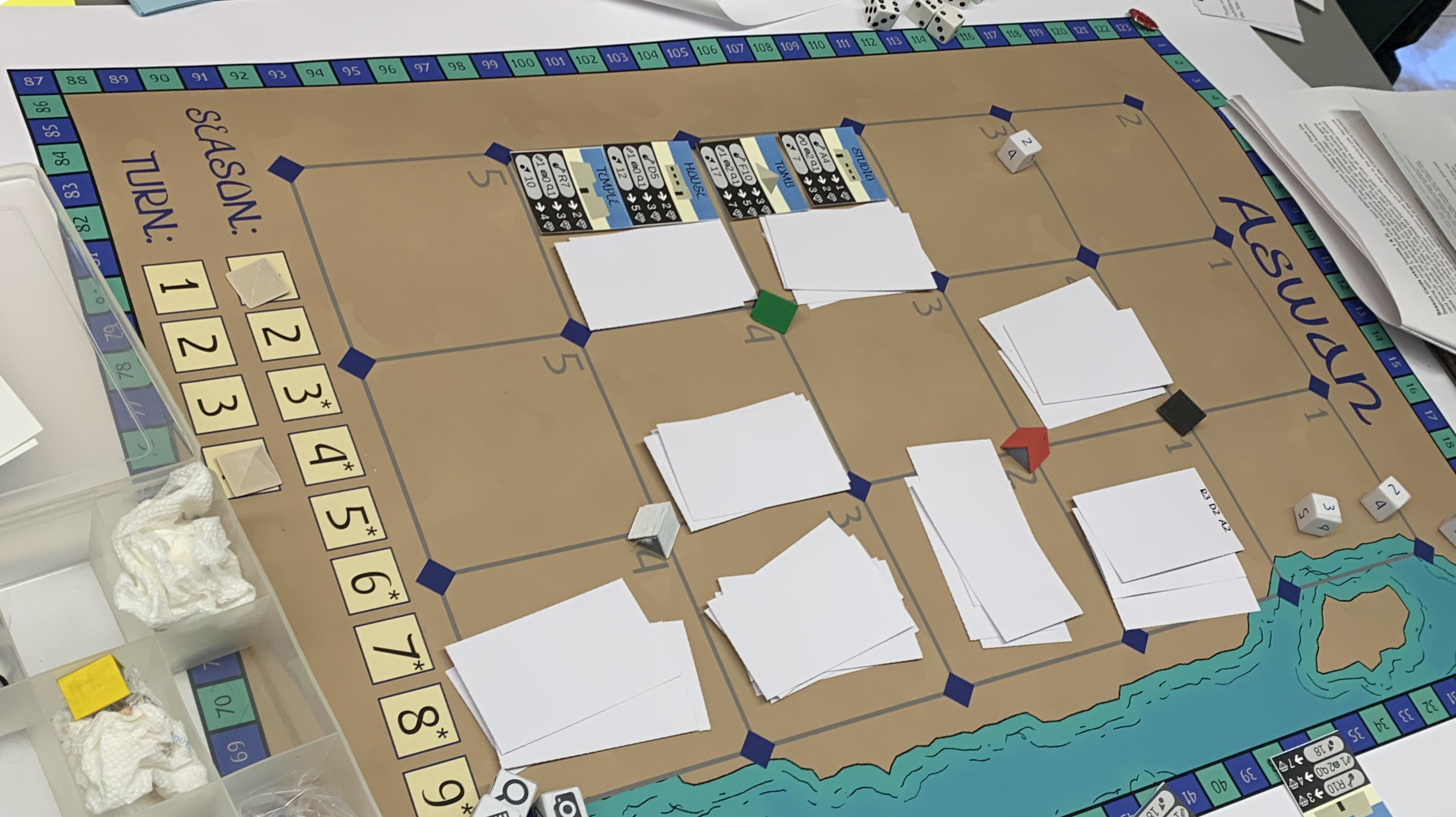 A game board for Aswan, showing one side of the Nile, with various dice and markers strewn about